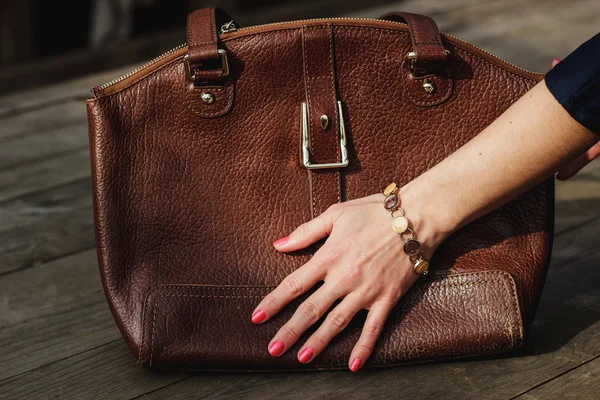 Mano femenina con brazalete sostiene un bolso de cuero marrón —  Fotos de Stock