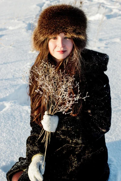 Mooie vrouw in een bontjas en bont hoed op een witte besneeuwde achtergrond — Stockfoto