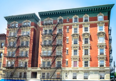 New York, USA -  July 12 2014: Red brick residential building on the corner of 5th Ave and W 120 st, with black metal emergency stairs.