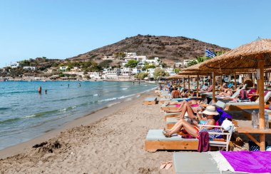 Kini, Syros, Yunanistan - 18 Eylül 2021: Güneşin tadını çıkaran yüzücülerle sahili görmek. Kini, Syros adasında, Kiklad adasında ve ünlü bir turist beldesinde pitoresk bir balıkçı köyüdür..