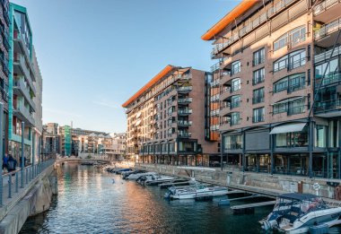Oslo, Norway - August 13 2022: Evening view of the waterfront of Tjuvholmen, with boats and buildings facing the canal. 