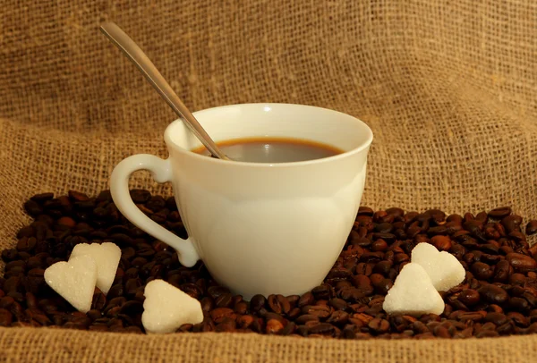 Una taza de café, grano tostado y azúcar en forma de corazones sobre la mesa —  Fotos de Stock