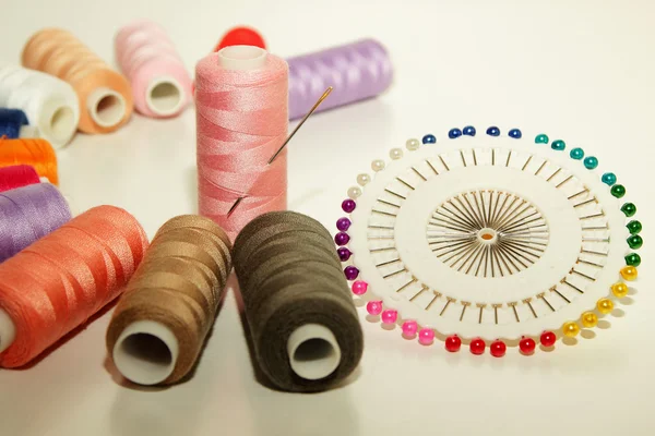 Colorful spools of thread, a needle to inject into a coil and a set of pins — Stock Photo, Image