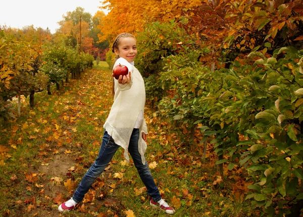 Chica bonita sosteniendo una manzana roja en la mano en el fondo del jardín de otoño —  Fotos de Stock