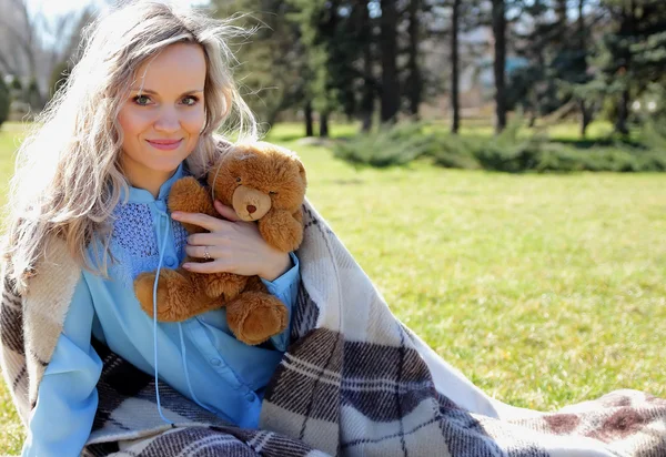 Mooi meisje met een teddybeer in haar hand en verpakt in een deken — Stockfoto