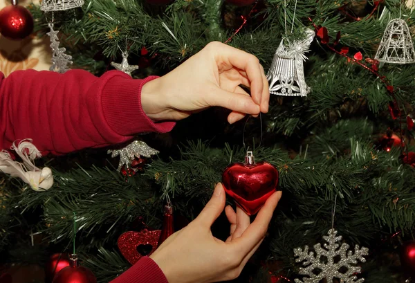 Menina pendura brinquedo na forma de coração em uma árvore de Natal — Fotografia de Stock