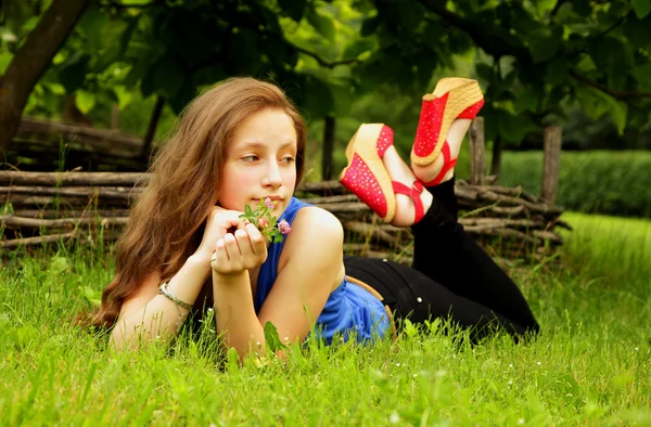 Güzel kız bahçede yeşil çim ile yatıyor ve mesafe içine görünüyor — Stok fotoğraf