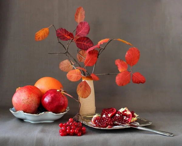 Rød frukt, bær, granatepler, oppdelt i deler og høstblader i en vase – stockfoto