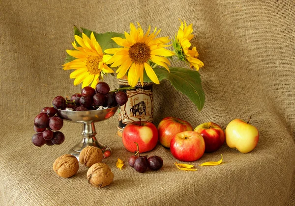 Äpplen, vindruvor, solrosor och nötter på säckväv bakgrund — Stockfoto