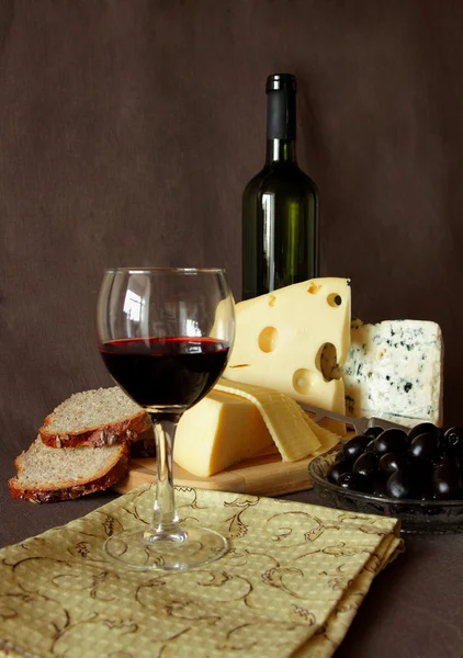 Bicchiere di vino rosso, bottiglia, olive e diverse varietà di formaggio — Foto Stock