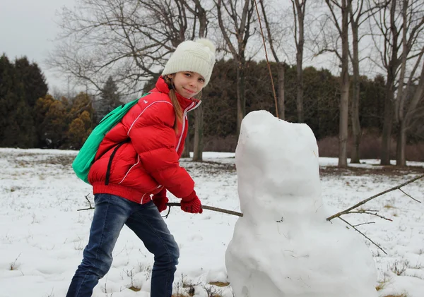 女の子は雪だるまを作って手の代わりに彼の棒を挿入します — ストック写真