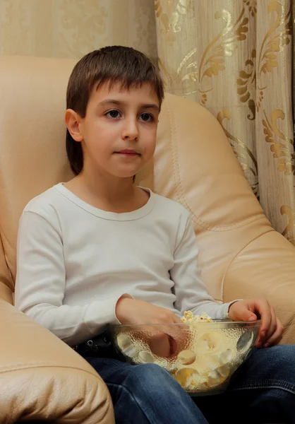 Niño comiendo palomitas de maíz sentado en el sofá viendo la televisión —  Fotos de Stock