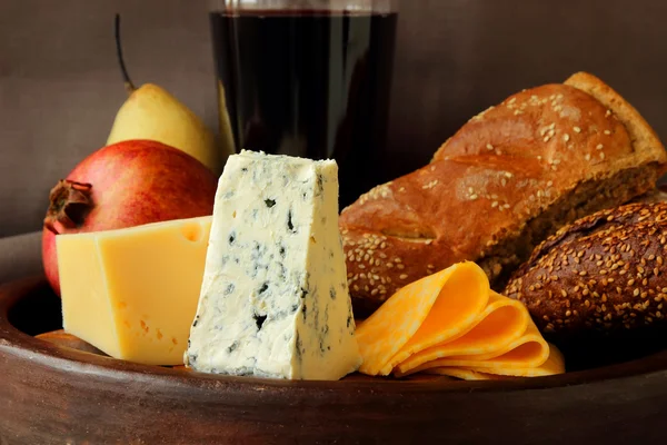 Varias variedades de queso, granada, pera y una botella de vino — Foto de Stock