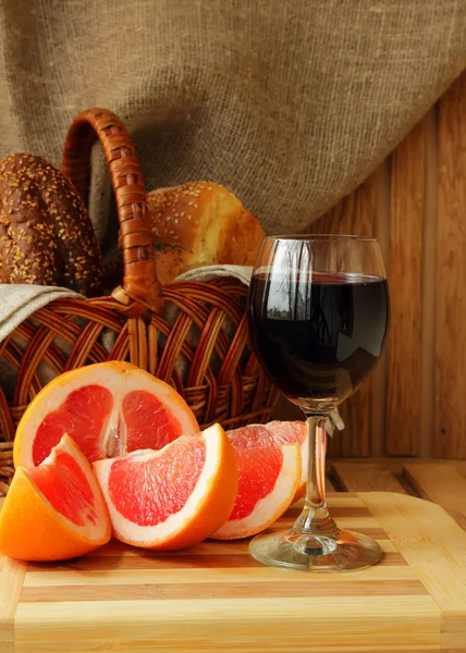Glass of wine, grapefruit and a basket of bread — Stock Photo, Image