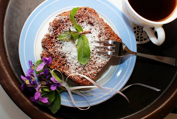 Slice of chocolate cake and a bouquet of violets — Stock Photo, Image