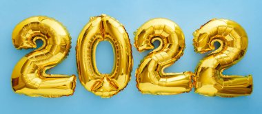 2022 yıllık altın balonlar mavi duvar arka planında düz yerde yatıyordu. Mutlu yıllar 2022 arifesi kutlamaları.