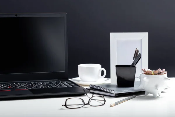 Рабочее место ноутбука Home Office. Рабочий стол со смартфоном ноутбука, блокноты ручки офисные поставщики чашки кофе напиток завод цветок. Белый стол стола на черном фоне. — стоковое фото