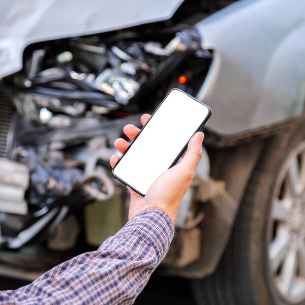 Мужчина держит в руках макет мобильного белого экрана телефона после автомобильной аварии. Звонок в страховую службу в веб-приложении на место аварии. Смартфон перед разбитой машиной. квадрат
