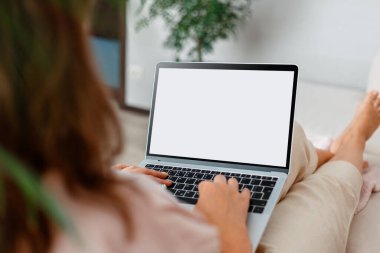 İnternetteki beyaz dizüstü bilgisayar ekranına bakan bir kadın e-uygulama sitesi ya da evdeki moovie 'ye bakıyor. Omzunun üstünden kadın ellerini klavyenin üzerine koy. Kanepede dizüstü bilgisayarlı bir kadın oturuyor.