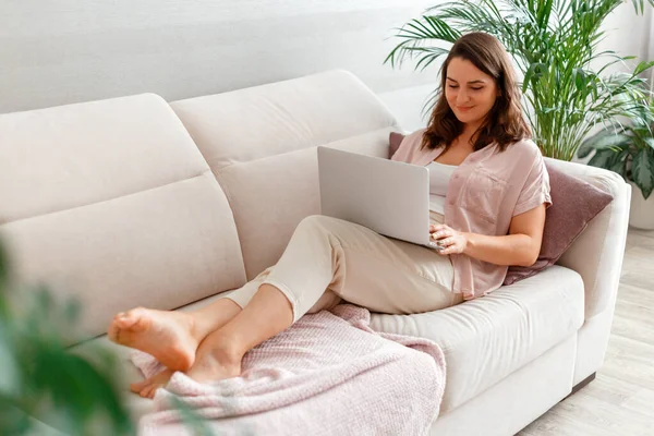 Kadın evdeki kanepede yatarken dizüstü bilgisayar kullanıyor. 30 'lu yaşlardaki sakin, beyaz kadın dizüstü bilgisayarda film seyrediyor. İnternetten alışveriş yapıyor ya da evdeki kanepede E-öğreniyor.