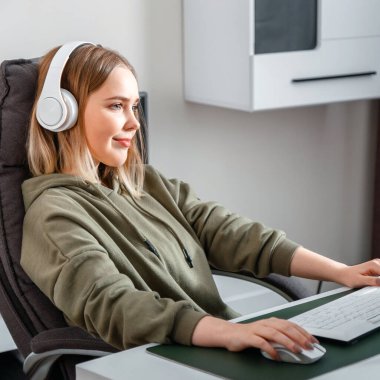 Genç kadın serbest çalışan oturma odasındaki bilgisayarla uzaktan kumandayla çalışıyor. Gündelik genç kız çevrimiçi eğitim dersleri alıyor. Yakın çekim kare portresi