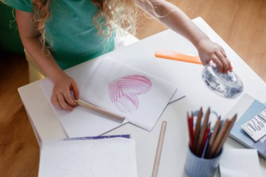 Küçük kız kağıda kırmızı kalp çiziyor. Çocuğun elleri anneler günü hediyesi olarak karta boyanmış kalp çiziyor. Sevgililer Günü 'nde kız sevgililer günü için kalp çizer..