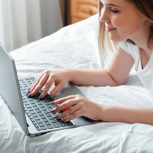 Happy teen dívka komunikuje on-line pracuje dálkově, studuje nebo plánuje svůj den používat počítač notebook v ložnici. Mladá žena úsměv psaní na klávesnici notebooku, zatímco ležel v posteli doma. Square — Stock fotografie