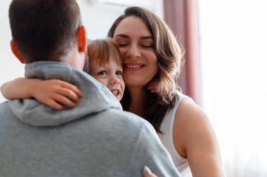Mutlu aile kucaklaşması. Küçük gülümseyen kız çocuğu, anne ve babasına ev içinde sarılıyor. Aile birlikte vakit geçirir, evde vakit geçirir.