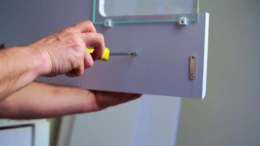 Erkek işçi Carpenter, tornavida aletine bağlı mobilyaları tamir ediyor. Kapatın. Yeni mobilya montajı yapan ya da evde mobilya tamiratı yapan adam. 