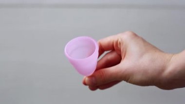 Adet bardağını tutan kadın. Beyaz arka planda regl fincanı kullanan kadın elleri görülüyor. Kadın mahrem hijyen dönemi sıfır atık ürünü. Kadın sağlığı kavramı.