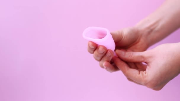 Femeie mână care deține ceașcă menstruală cu spațiu de copiere. Mâinile de sex feminin arată folosind cupa menstruală izolată pe fundal de culoare roz. Perioada de igienă intimă feminină zero deșeuri produse. Conceptul de sănătate pentru femei. — Videoclip de stoc