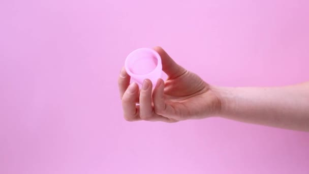Nő kéz gazdaság menstruációs csésze elszigetelt színes rózsaszín háttér. Női intim higiéniai időszak termékek, a menstruációs csésze. Női egészségügyi koncepció, nulla hulladék. — Stock videók