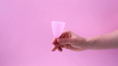 Kadın eli, menstrüal fincanı pembe arka planda kırmızı tüy ile gösterir. Adet bardağını tutan kadın. Kadın mahrem hijyen dönemi sıfır atık ürünü. Kadın sağlığı kavramı.