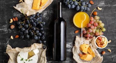 Red wine bottle mockup. Wine and cheese composition. Gastronomy Ingredients different cheese grapes honey on dark concrete background. Long web banner