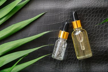 Collagen Serum or hyaluronic serum in dropper on black color crocodile skin texture background with palm leaves. Skincare cosmetic product bottle. Cosmetics health face skin beauty