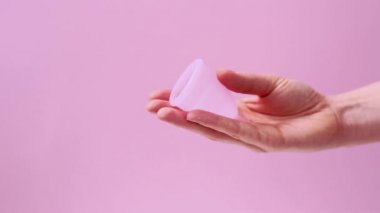 Adet bardağını tutan kadın. Kadın eli, pembe arka planda izole edilmiş adet bardağı kullandığını gösteriyor. Kadın mahrem hijyen dönemi sıfır atık ürünü. Kadın sağlığı kavramı.