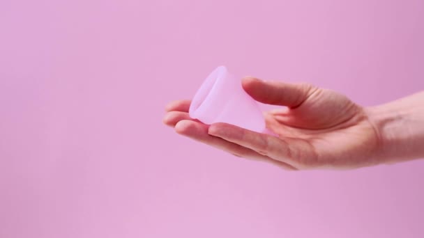 Mano de mujer sosteniendo copa menstrual. Las manos femeninas muestran el uso de copa menstrual aislada en el fondo de color rosa. Higiene íntima femenina período cero productos de desecho. Concepto de salud femenina. — Vídeos de Stock