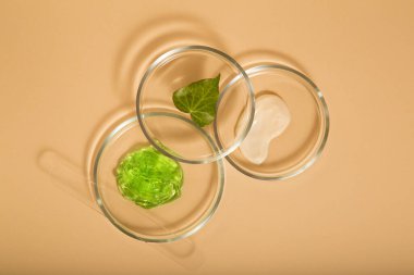 Bej arka planda petri kabında kozmetik cilt ürünleri. Aloe jeli, nemlendirici krem doğal kozmetik ürünleri laboratuvar camları. Üst görünüm