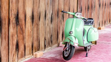 Green scooter against old house. wood wall mossy surface of building as background. Urban street in Thailand, Asia. Moped parked at moldy wood wall. Asian lifestyle and popular transport.