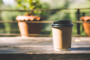 Paper cup of coffee on wooden table against blurred nature background.