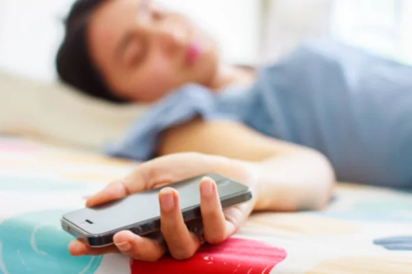 Arka plan bulanık. Akıllı bir telefon tutan Uyuyan Genç Kadın