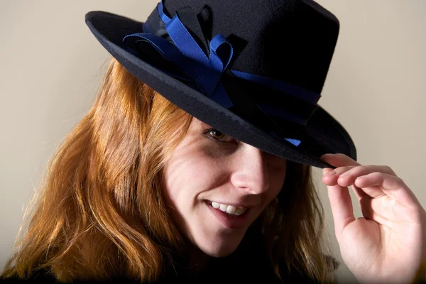 Pelirroja sonriendo en sombrero negro tocando ala — Foto de Stock
