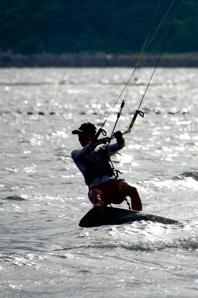 Hombre cometa surfista retroiluminado cerca de la orilla boscosa —  Fotos de Stock