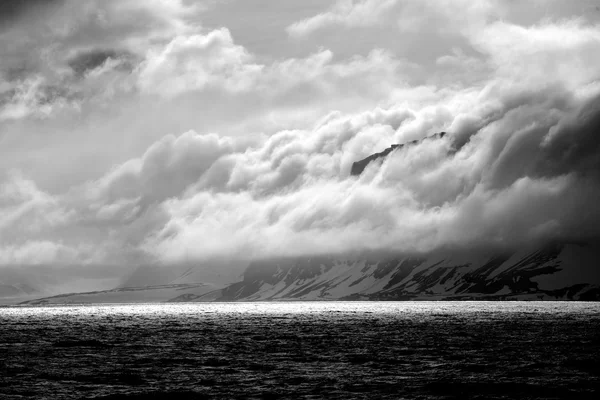 Black and white cliff beside backlit ocean — Stock Photo, Image