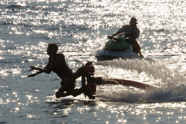 De dalende vooruit Flyboarder naast backlit jetski — Stockfoto