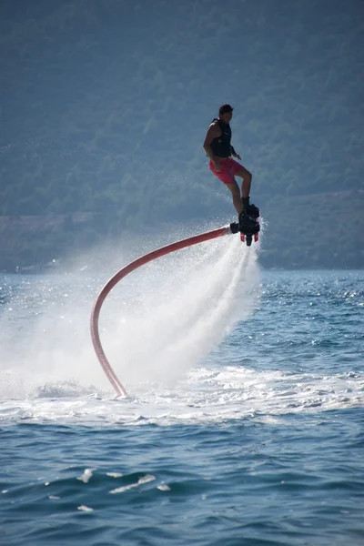 Flyboarder en pantalones cortos de color rosa en espiral sobre spray —  Fotos de Stock