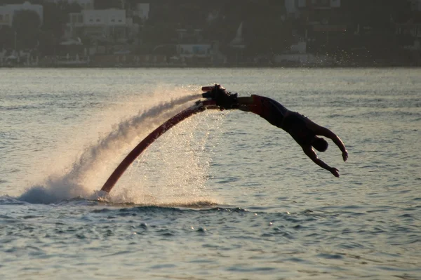 Flyboarder i semi-cirkulär dyk i bakgrundsbelyst vågor — Stockfoto