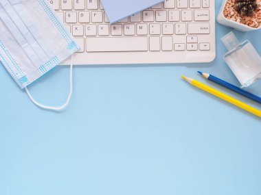 Üst manzara, düz yatak, ofis mavisi masa üstü kalem, klavye, el dezenfektanı alkol jeli, tıbbi yüz maskesi ve kaktüslü. Metnin için alanı kopyala. İş, eğitim ve ev kavramından çalışma