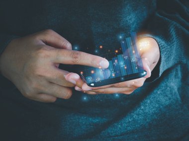 İş adamı ekrandaki 2022 çubuk grafik simgesine bakmak için akıllı telefonu kullanıyor. İş büyütme planı. Finansal iş planlama kavramı