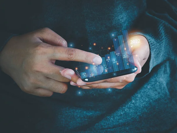 İş adamı ekrandaki 2022 çubuk grafik simgesine bakmak için akıllı telefonu kullanıyor. İş büyütme planı. Finansal iş planlama kavramı